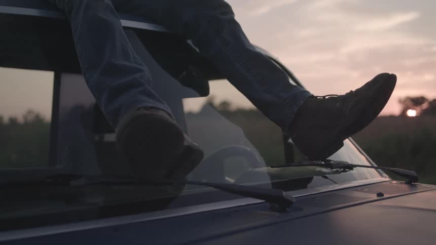 A man is sitting on the roof of a truck with his feet resting on the window