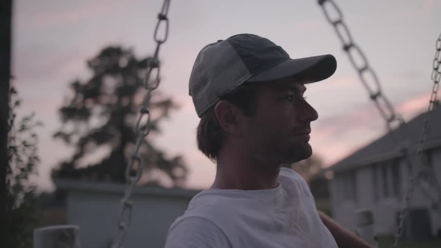 A man sits on a swing in the yard