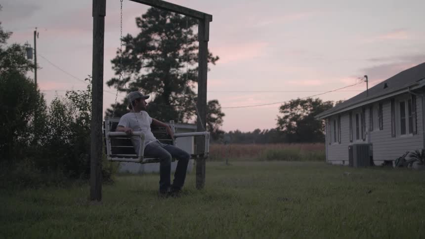A man is sitting on a swing in his yard