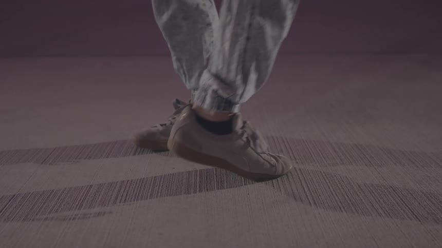 A person wearing lightcolored jeans and sneakers is captured shuffling on a textured surface