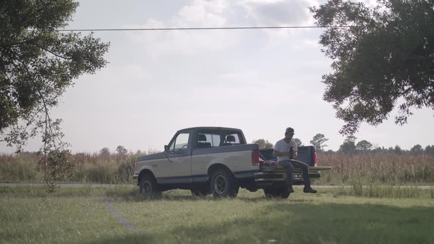 Man sitting in the back of a pickup truck drinking from a bottle during the day