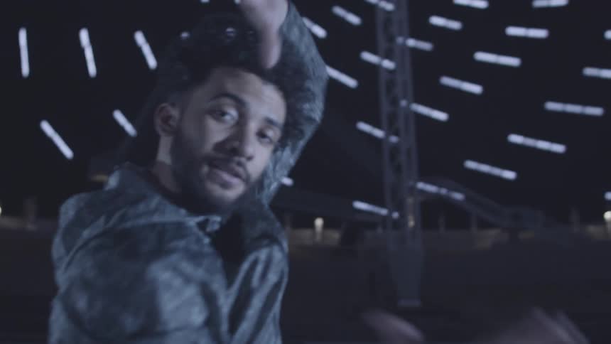Man in jacket dancing in indoor space with lighting and making hand gestures