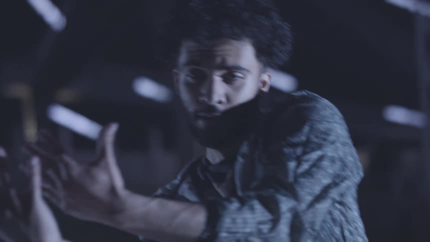 A man dances on a stage using expressive hand gestures and fluid body movements