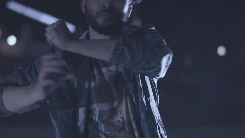 Young curly haired man in a night setting dancing moving his hands
