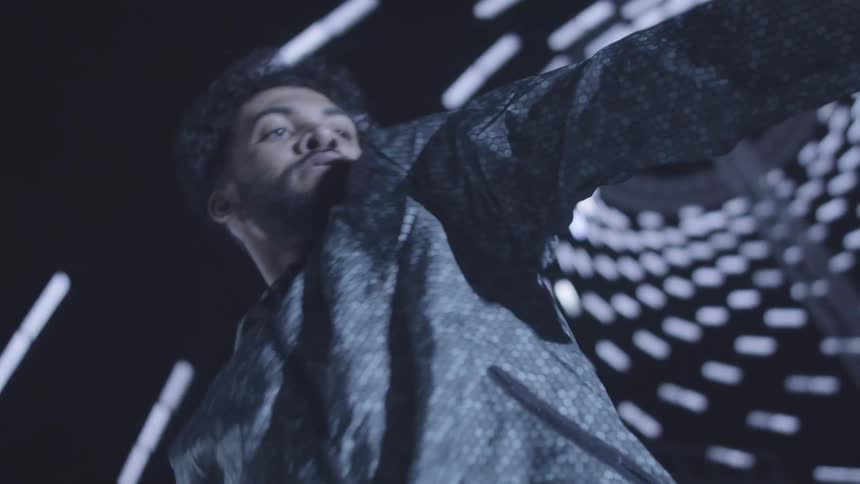 A man with afro hair and a bearded face dances on a stage