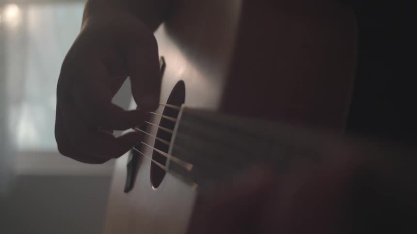 A man is playing a guitar by the window