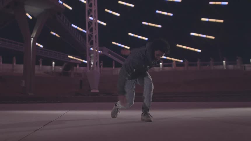 A young man with afro hair dances joyfully on a stage illuminated by a series of bright lights