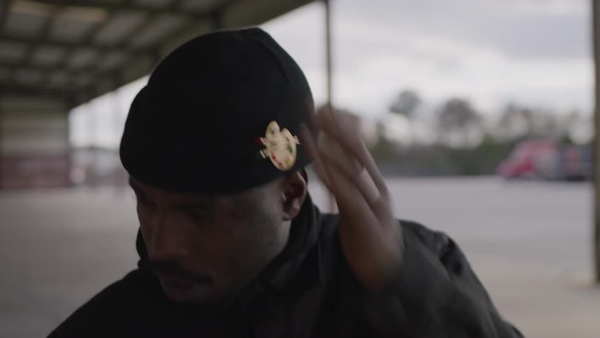 A man in a black beanie is adjusting his cap and glancing around while standing in a covered outdoor structure