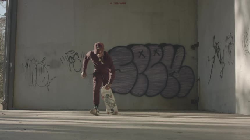 A man runs and hops onto his skateboard outdoors at midday near a building wall covered with street art