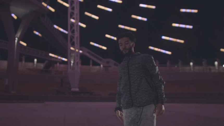 A black man dances on stage moving his body and arms rhythmically beneath a series of lights