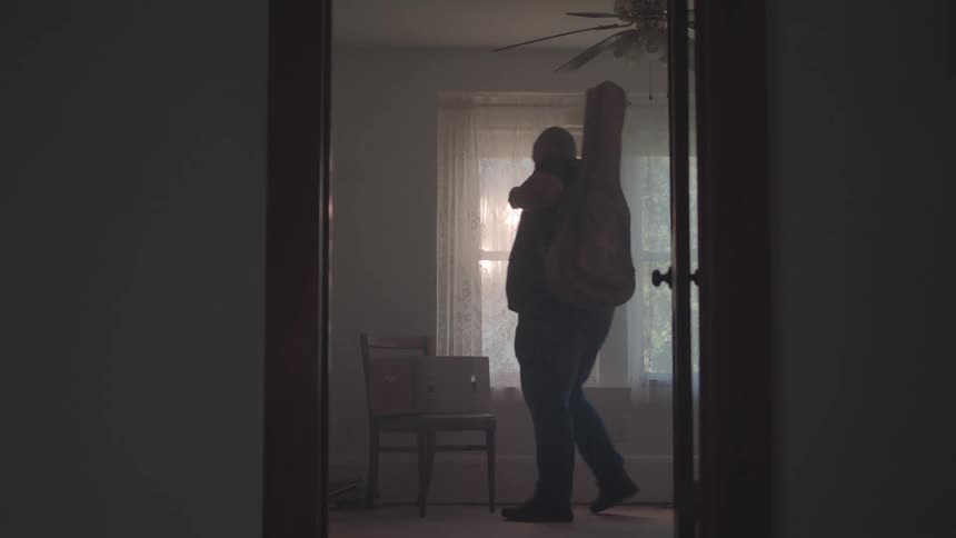 A man picks up a cardboard box off of a chair and walks out of the room