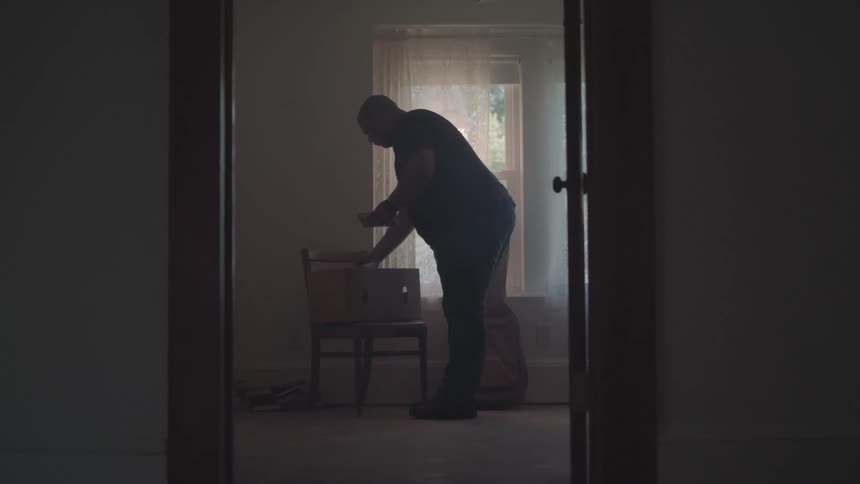 Man puts items in a box sitting on a chair near the window