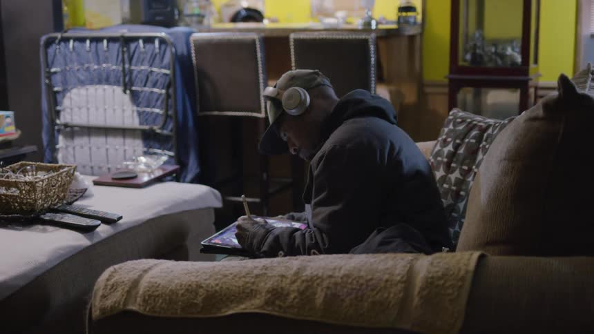 Man with headphones sitting on a sofa and drawing on a tablet