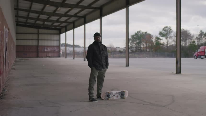 Man standing in a coat and hat next to a skateboard