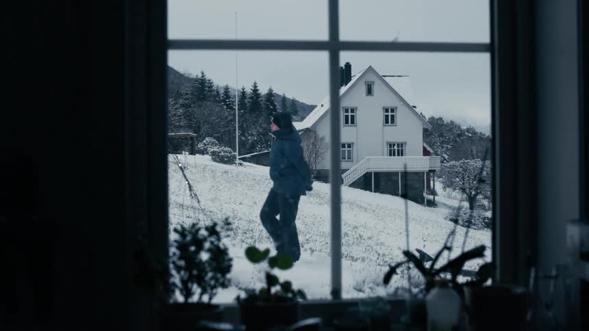 A man visible through a window at midday wears winter clothing as he pulls a sled behind him across the snowcovered ground