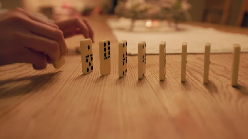 Hand stacking dominoes on top of a wooden table