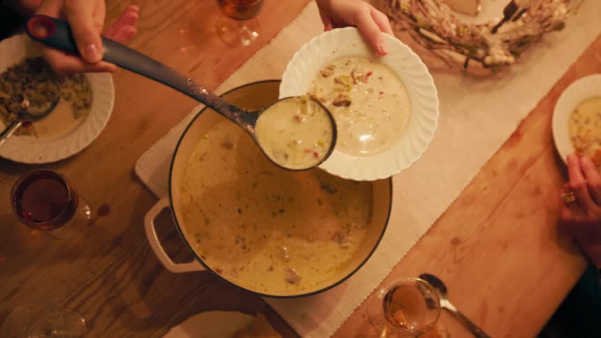 Pair of hands pouring soup into a plate and handing it to another person