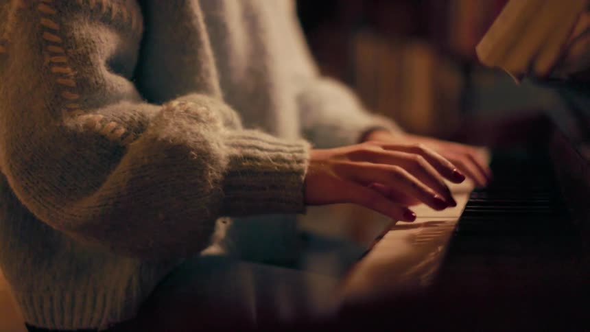 A woman wearing a sweater is playing the piano
