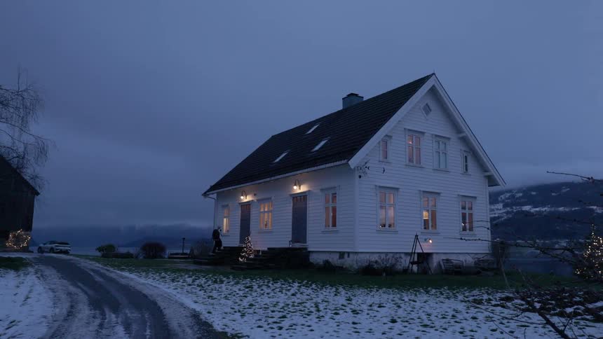 Person walking towards the door of a house in a snowy environment at dusk