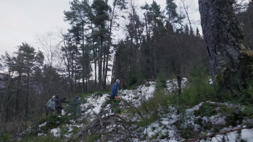 A father carries an axe while walking up a snowcovered hillside with his family