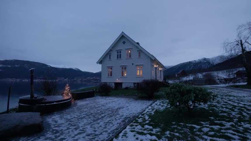 House in a rural area on the edge of a lake with a christmas tree with decorated lights at dusk