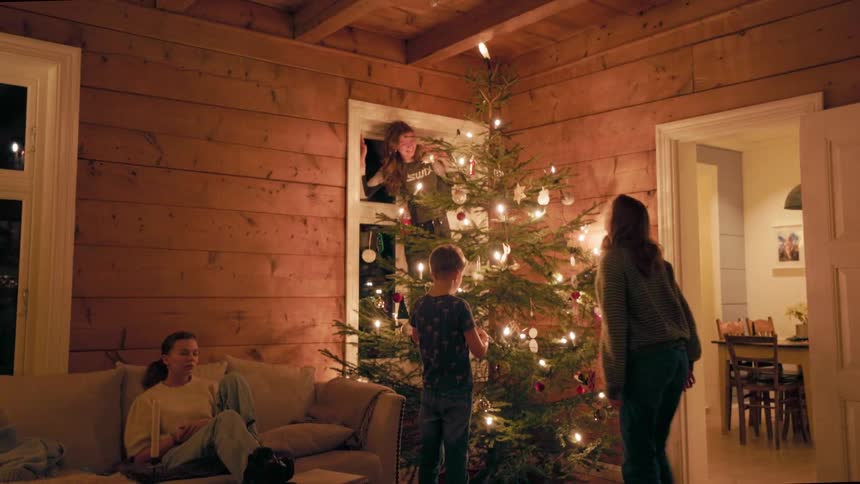 Mother with her three children next to a lit christmas tree in the corner of the living room at night