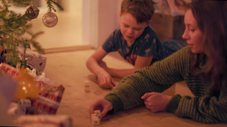 A little boy and a woman are lying on the floor next to a christmas tree stacking dominoes