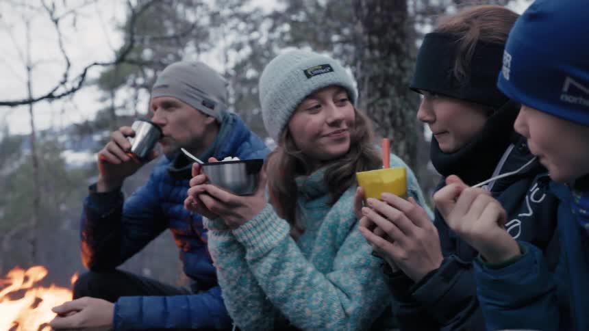 Family with two young children eating together on a camping trip in the woods
