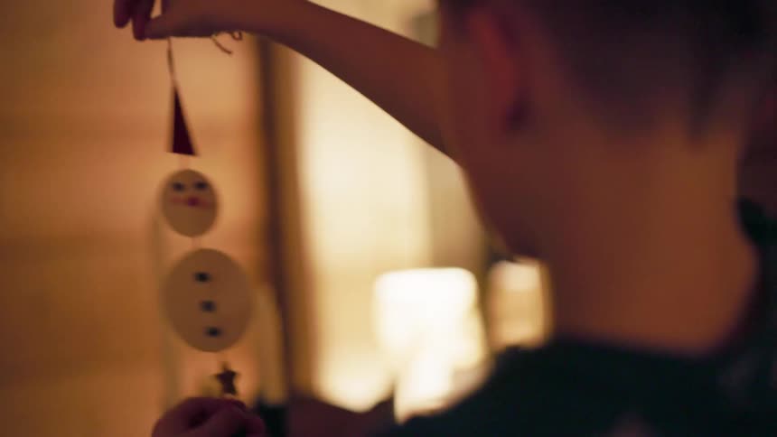 A child holds a snowman ornament in a warmly lit room