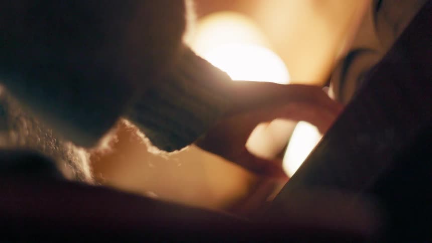 A hand wearing a knitted sweater is gently playing piano with a warm light illuminating the background
