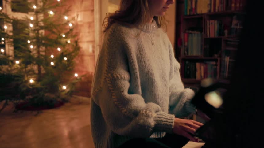 Woman sitting in a room at night with a christmas tree playing the piano