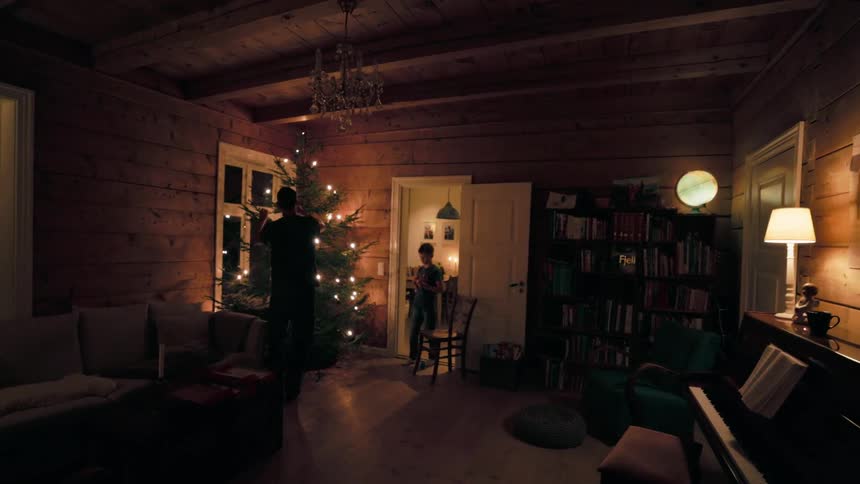 Father and son are in a warmly lit woodpaneled room with a decorated christmas tree bookshelves and a piano