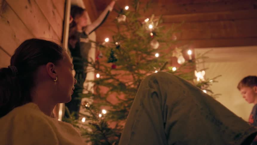 A family decorates a christmas tree in a cozy warmly lit cabin