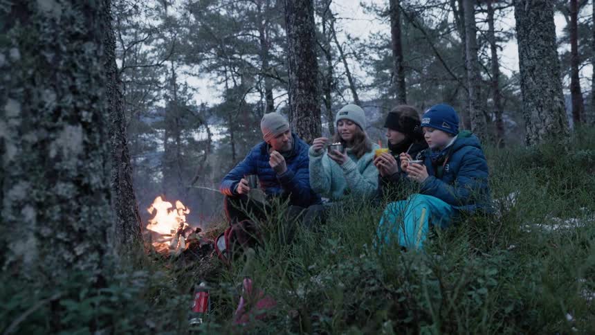 A father son and two daughters are enjoying hot soup by the campfire on a fall evening