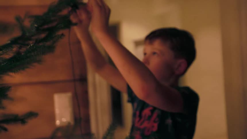 A child hanging lights on a christmas tree indoors