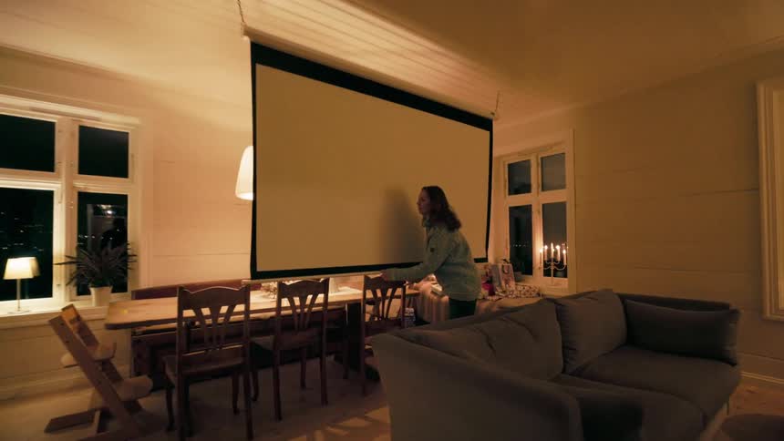 A woman in a living room lowering a projector screen