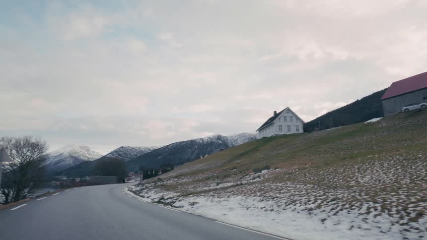 Houses at the foot of a mountain on the edge of a road next to a lake with mountains on the horizon