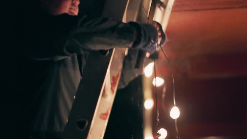 A man is hanging christmas lights on a ladder