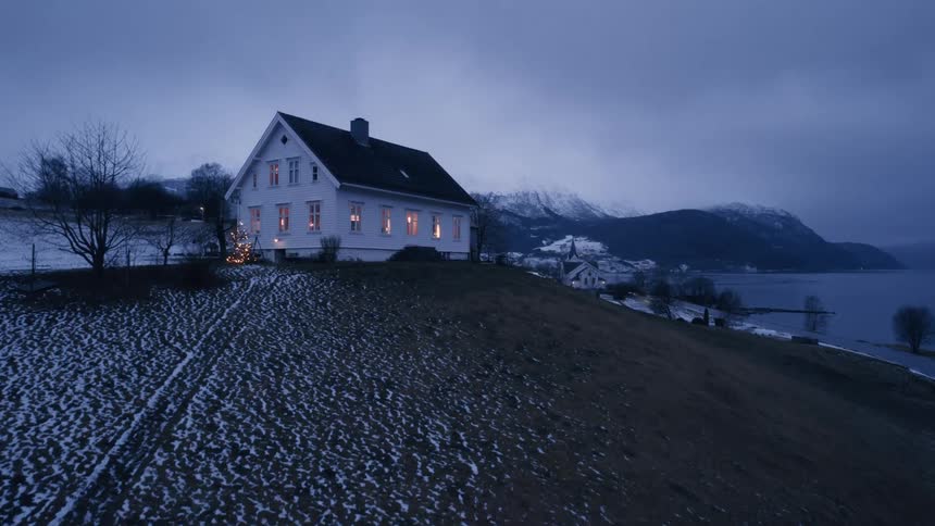 A building sits on a hill near the coast surrounded by snow from winter under a cloudy evening sky
