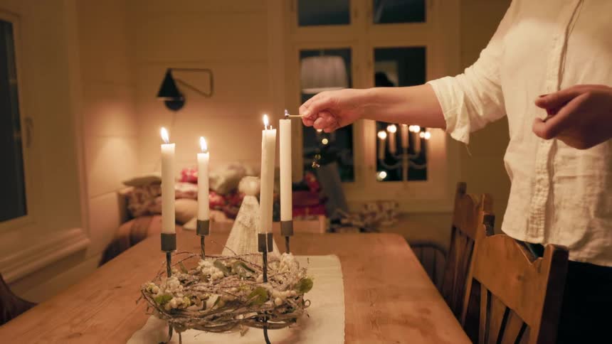 Person with match lighting candles on top of a dining table