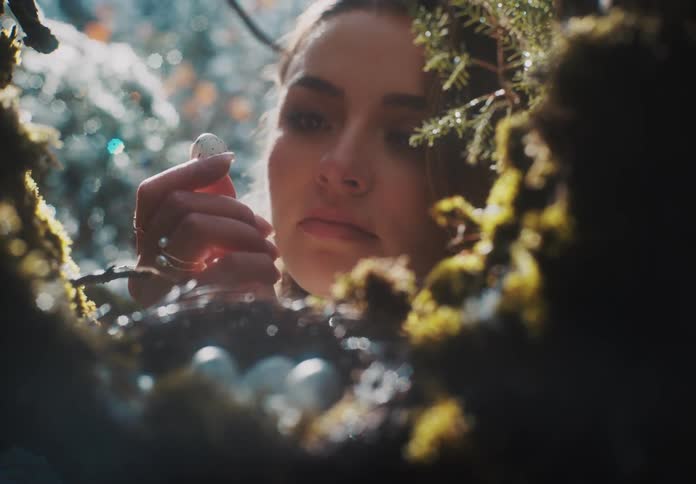 Woman picks up a white egg with black speckles from a nest and examines it closely