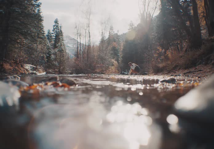 Woman walking and crouching next to a stream in the forest