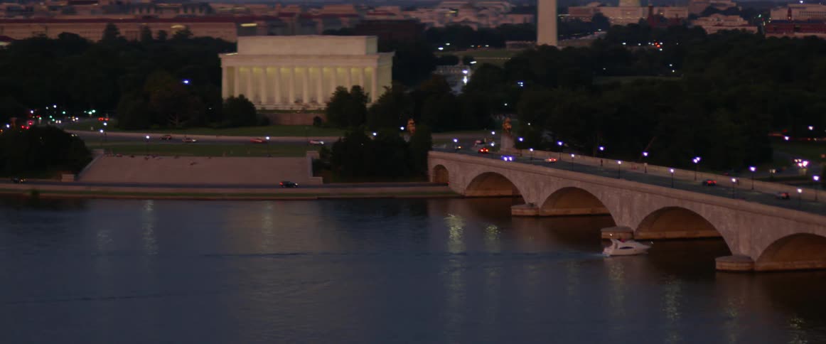 Vehicles drive on a city bridge while a boat passes beneath