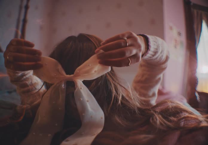 A woman lies on the bed touching the bow head tie used to tie her hair