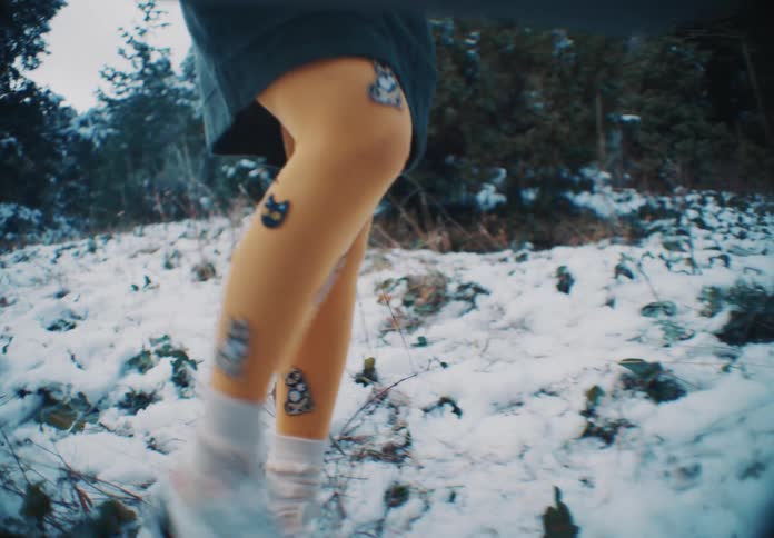 Woman wearing a dress and brightly colored tights walks across the snow in the forest on a winter day