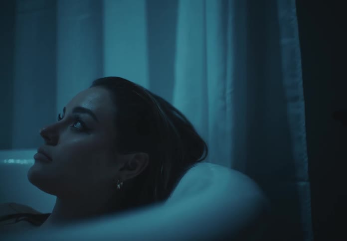 Woman looks up while soaking in the bathtub in a dimly lit bathroom