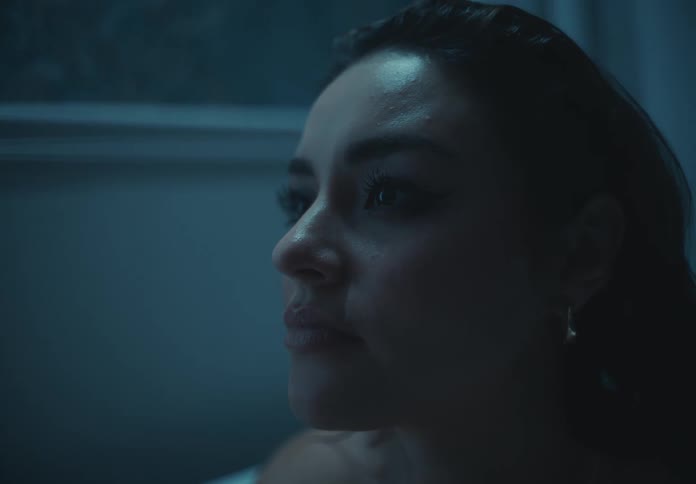 The face of a woman who is sitting in a bathtub while looking forward with sad expressions and with her hand on her face