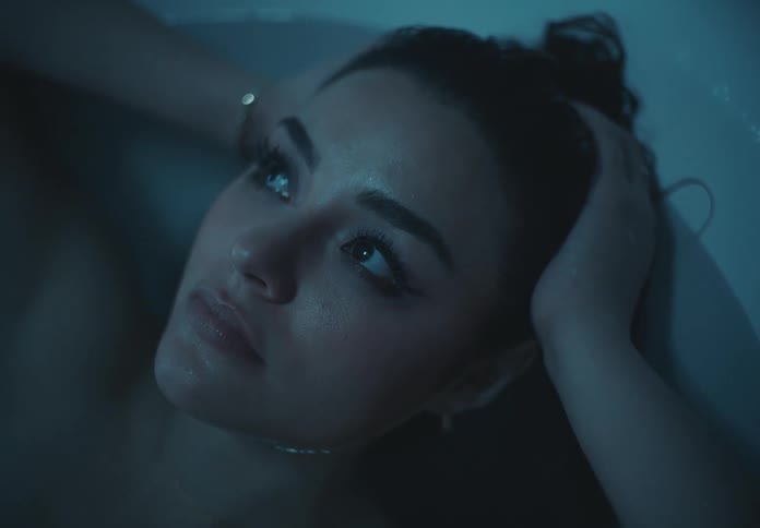 A young woman lies in a bathtub with both hands on her head lost in deep thought