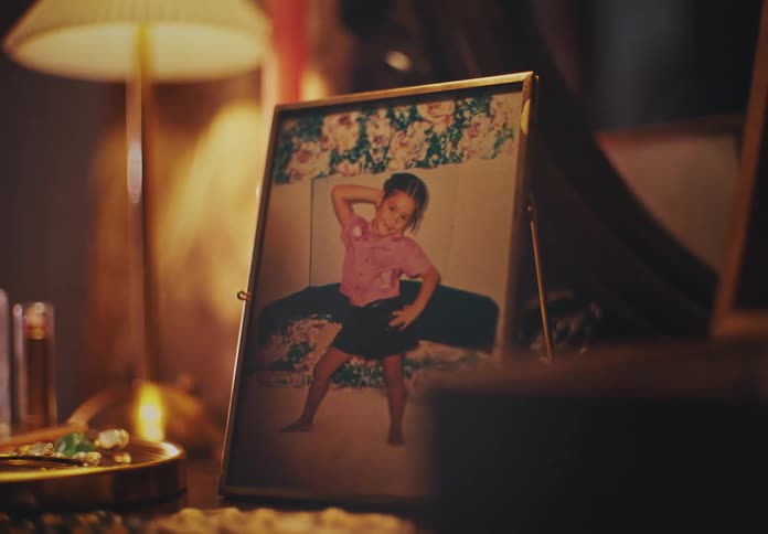 A photo portrait of a little girl who is posing with her hand on her head while standing on a bed