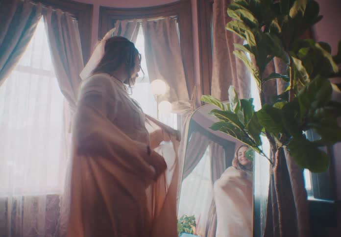 A woman stands in front of a mirror checking out her dress with a smile and excitement on her face